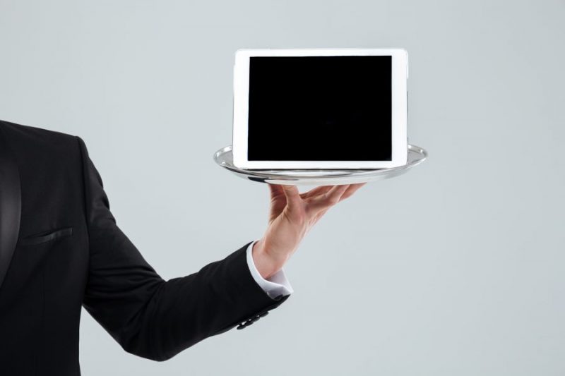 an ipad tablet point of sale being held on a silver tray by a male waiter in a black suit to show how great iPad POS software is for restaurants