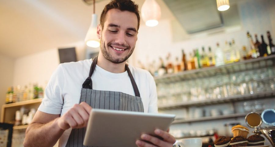 Happy male barista using digital tablet at cafe